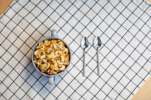 A plate of cashew nuts on a nice napkin and two spoons next to it. Delicious and healthy food for a snack. There is a place for the text.