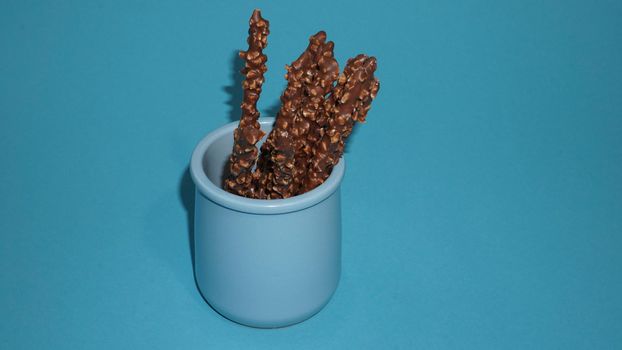 Chocolate crispy sticks with hazelnut sprinkles on a blue background.