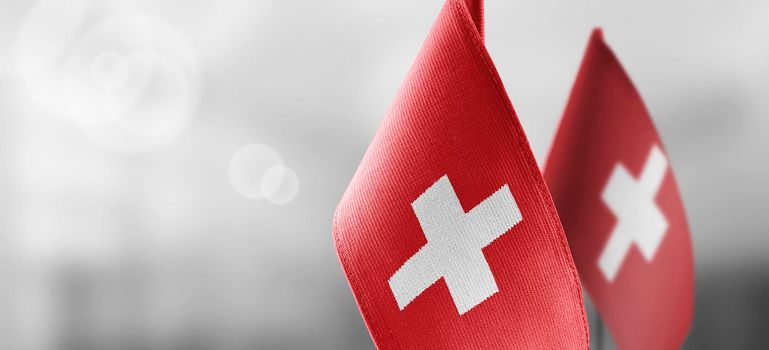 Small national flags of the Switzerland on a light blurry background.