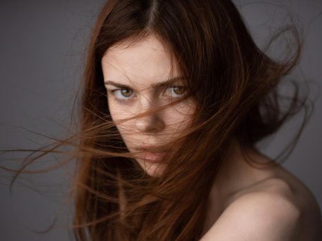 Offended look of a red-haired woman on a gray background bared shoulders close-up. High quality photo