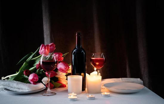 Romantic Candlelight Dinner for Two Lovers. Set of tableware with bouquet of tulips, wine and candles, dark background