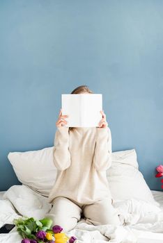 Woman sitting on the bed wearing pajamas covering her face with a book, mock up design