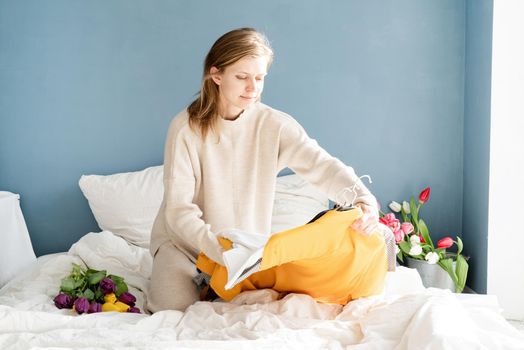 Young smiling woman organizing clothes sitting on the bed at home