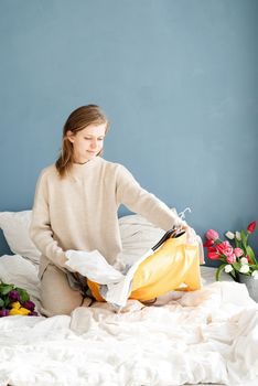 Young smiling woman organizing clothes sitting on the bed at home