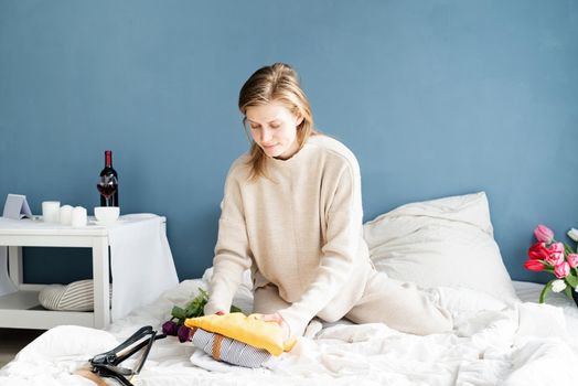 Young smiling woman organizing clothes sitting on the bed at home