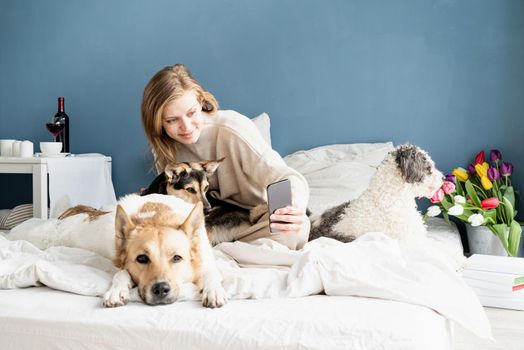 Happy young woman sitting in the bed with her dogs, taking selfie