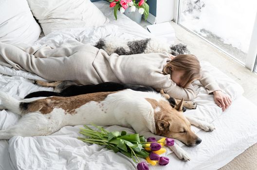 Sleeping young woman wearing pajamas lying in the bed with her dogs