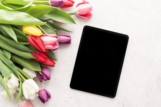 Spring concept. Bouquet of colorful tulip flowers and mock up digital tablet top view flat lay