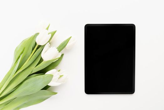 Spring concept. Bouquet of white tulip flowers and mock up digital tablet top view flat lay