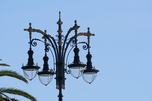old city lights with multiple shades and patterned wrought on the background of blue sky and the leaves of palm trees