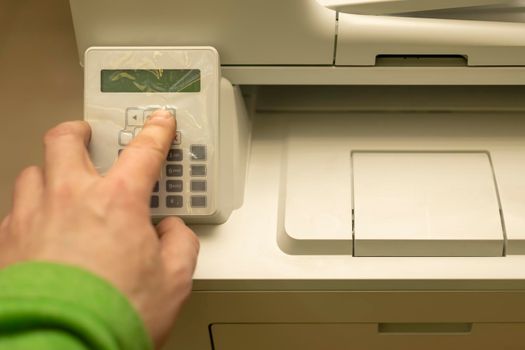 the hand of a person, an office worker, presses the buttons on the control panel of a printer, copier, or multifunction device