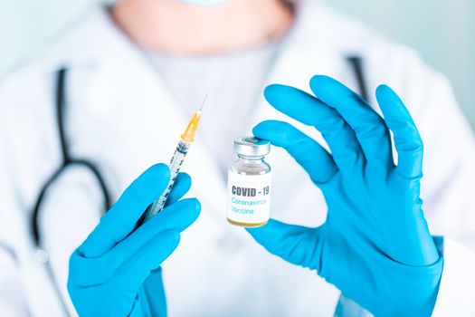 Woman doctor or nurse in uniform and gloves wearing face mask protective in lab, holding medicine vial vaccine bottle with COVID-19 Coronovirus vaccine label