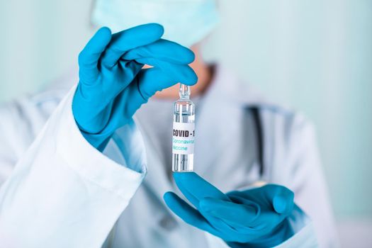 Woman doctor or nurse in uniform and gloves wearing face mask protective in lab, holding medicine vial vaccine bottle with COVID-19 Coronovirus vaccine label