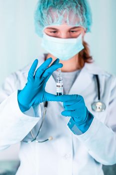 Woman doctor or nurse in uniform and gloves wearing face mask protective in lab, holding medicine vial vaccine bottle with COVID-19 Coronovirus vaccine label