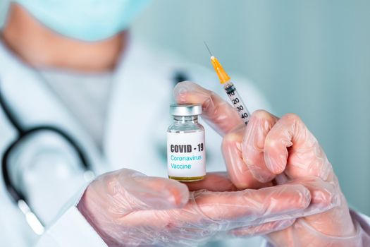 Woman doctor or nurse in uniform and gloves wearing face mask protective in lab, holding medicine vial vaccine bottle with COVID-19 Coronovirus vaccine label