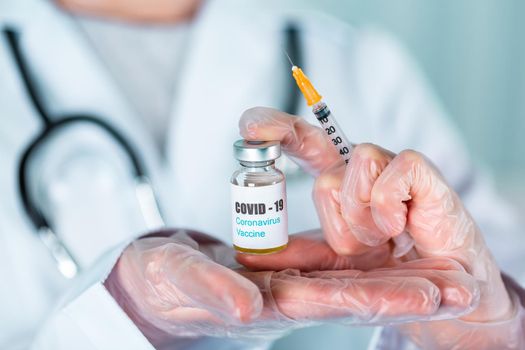 Woman doctor or nurse in uniform and gloves wearing face mask protective in lab, holding medicine vial vaccine bottle with COVID-19 Coronovirus vaccine label