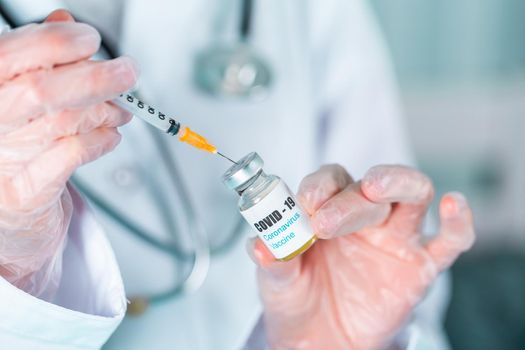 Woman doctor or nurse in uniform and gloves wearing face mask protective in lab, holding medicine vial vaccine bottle with COVID-19 Coronovirus vaccine label