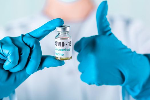 Woman doctor or nurse in uniform and gloves wearing face mask protective in lab, holding medicine vial vaccine bottle with COVID-19 Coronovirus vaccine label