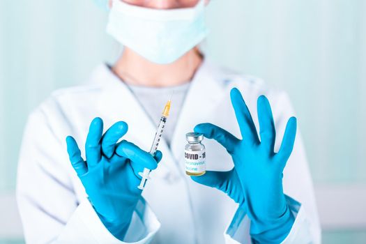 Woman doctor or nurse in uniform and gloves wearing face mask protective in lab, holding medicine vial vaccine bottle with COVID-19 Coronovirus vaccine label