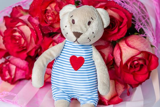 A bouquet of red roses in a gift paper package and a soft toy bear with an embroidered heart. The concept of a gift to a woman for any event, a symbol of love, valentine's day