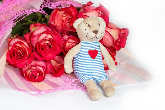 A bouquet of red roses in a gift paper package and a soft toy bear with an embroidered heart. The concept of a gift to a woman for any event, a symbol of love, valentine's day