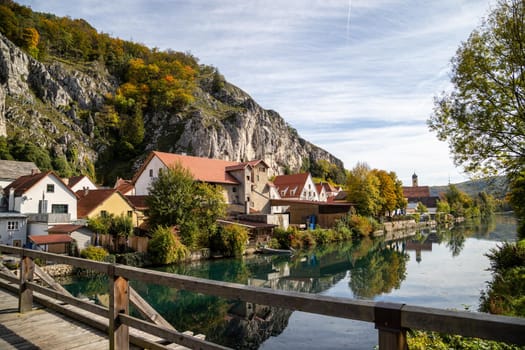 Idyllic view at the village Markt Essing in Bavaria, Germany with the Altmuehl river, high rocks in background and a wooden bridge in the foreground on a sunny day in autunm