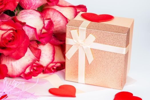 A bouquet of red roses in gift paper packaging and a small box with a gift on a white background. The concept of a gift to a woman for any event, a symbol of love