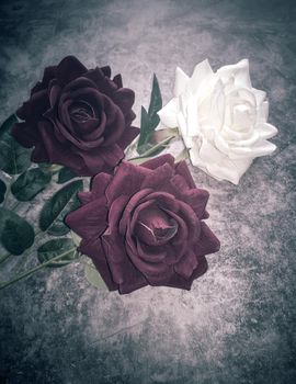 On a dark background, three beautiful artificial roses, two red and one white.