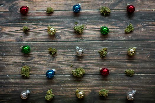 Tiny Colorful Christmas Balls and Cannabis Nugs on a Wooden Background in a Diagonal Pattern