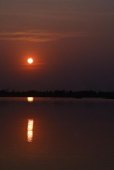 Vertical picture of the lakeside landscape with orange sky and beautiful sunset.