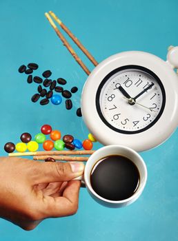 Man hand holding espresso cup with alarm clock on confectionery and sweet candy background.