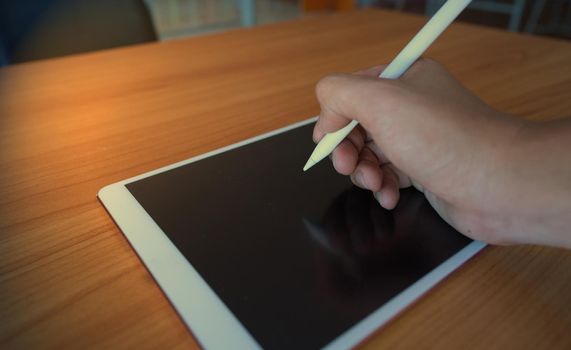 A man writing on the tablet with an electronic pencil on a wooden table