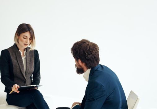 A man in a blue jacket sits opposite a woman in a suit on a light background indoors. High quality photo