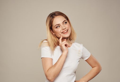 Pretty blonde in a white T-shirt on a beige background touches her face with her hand cropped view. High quality photo