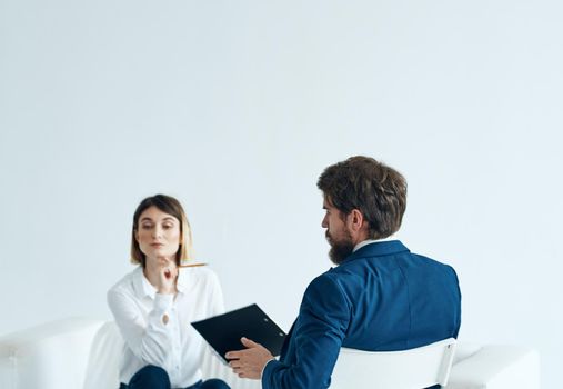 A woman psychologist with documents sits on the couch and a man on a chair in a suit. High quality photo