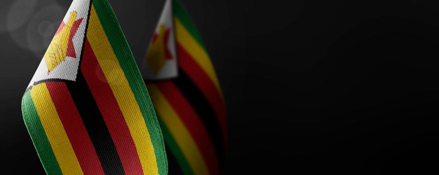 Small national flags of the Zimbabwe on a dark background.