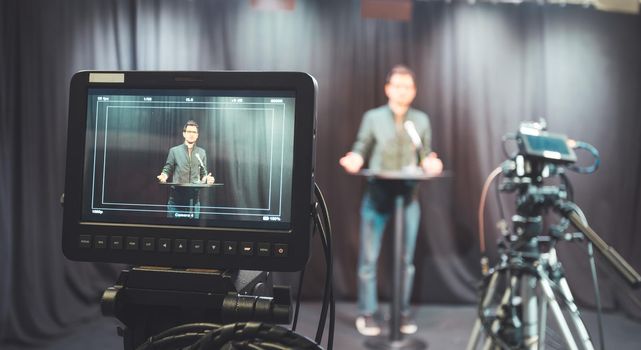 Male journalist in a television studio talks into a microphone, film cameras