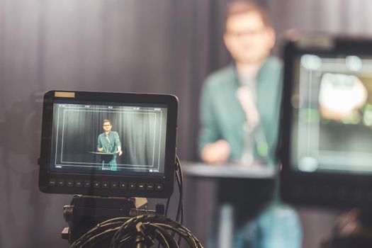 Male journalist in a television studio talks into a microphone, film cameras