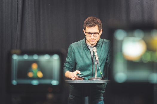 Male journalist in a television studio talks into a microphone, film cameras