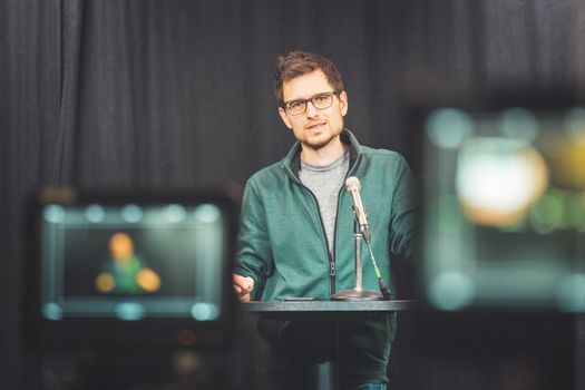 Male journalist in a television studio talks into a microphone, film cameras