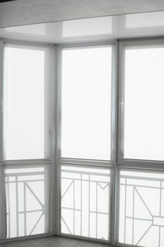 White fabric roller blinds on the plastic window on a balcony in the living room with a reflection in a stretch ceiling