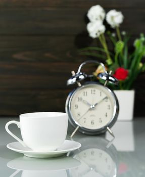White coffee cup and alarm clock with Artificial flower vase bouquet on table