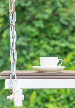 Coffee cup on seat suspended by chains in green garden relaxation time