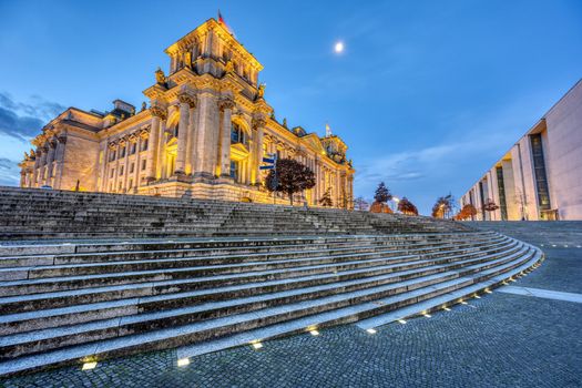 The illuminated Reichstag in Berlin seen from the river Spree at dawn