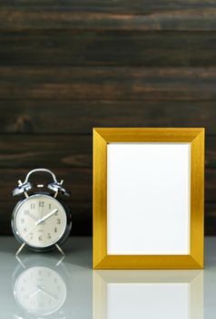 Mockup with blank golden frame and alarm clock on table