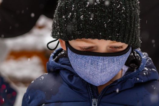 Cute blue-eyed boy with a black hat an a  face mask in the snow