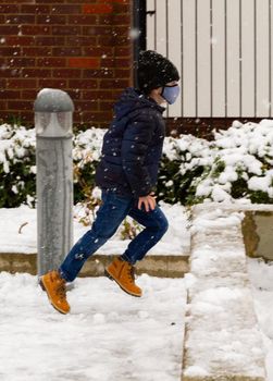 A cute boy wearing a black hat and a blue face mask running in the snow