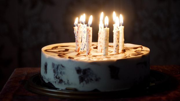Birthday cake with colorful burning candles in dark.