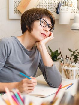 Woman with short hair cut is drawing in notebook. Calming hobby, antistress leisure. Artist at work. Cozy workplace.