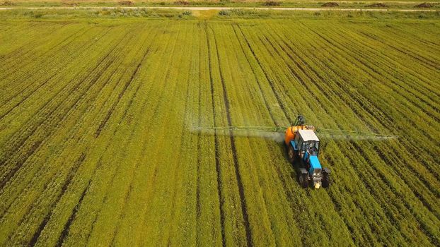 Aerial view tractor spraying the chemicals on the large green field. Spraying the herbicides on the farm land. Treatment of crops against weeds.
